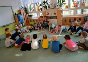 Dzieci siedząc na dywanie naśladują ruchem wałkowanie ciasta .
