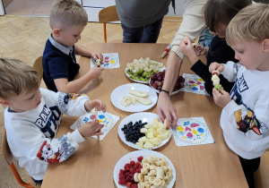 Dzieci przygotowują owocowe szaszłyki.