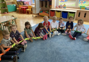 Dzieci siedzą na dywanie i trzymają gumę sensoryczną.