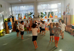 Dzieci ćwiczą w strojach gimnastycznych założonych na lewą stronę. Poruszają się podskokami do tyłu.