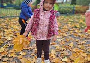 Dziewczynka stoi i prezentuje swój bukiet z liści.