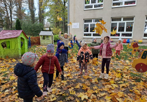 Dzieci podrzucają liście do góry.