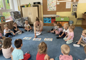 Dzieci siedzą na dywanie i odpowiadają na pytania nauczyciela.