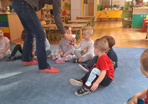 Dzieci siedzą na dywanie i witają się z Kicią Kocią.