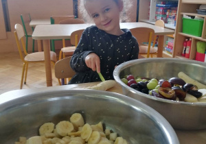 Dziewczynka uśmiecha się do zdjęcia, w czasie krojenia owoców.