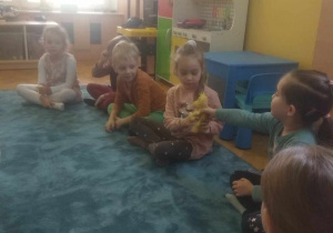 Dzieci siedząc w kole podają sobie zabawkę.