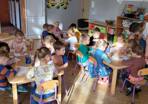 Dzieci siedzą przy stolikach i kolorują kalosze.