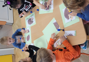 Dzieci składają pocięty obrazek przedstawiający jeża.