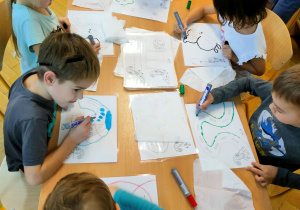 Dzieci siedzą przy stoliku. Rysują wzory na kartach graficznych mazakami suchościeralnymi.