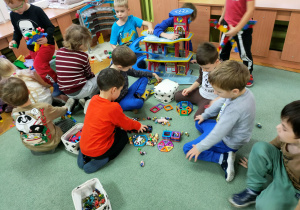 Dzieci zgrupowane na dywanie bawią się różnymi zabawkami.