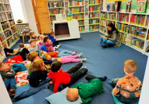 Dzieci w skupieniu słuchają bajki czytanej przez panią bibliotekarkę.