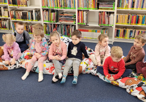 Dzieci siedzą na kolorowych poduszkach i czekają na rozpoczęcie zajęć.