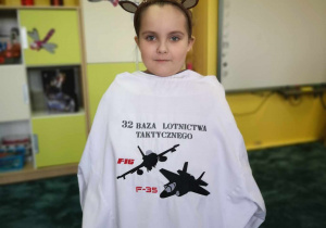 Dziewczynka pozuje z koszulą kucharską 32 Bazy Lotnictwa Taktycznego.