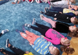 Dzieci leżą na dywanie i pobudzają wyobraźnię w czasie zajęć.