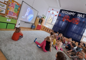Dzieci siedzą na dywanie i oglądają prezentację o czystym powietrzu