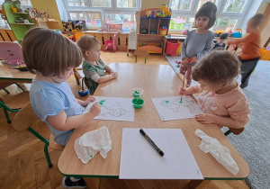 Dzieci siedzą przy stolikach i malują farbami