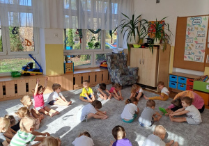 Dzieci siedzą na dywanie z siadzie płaskim i robią skłon.