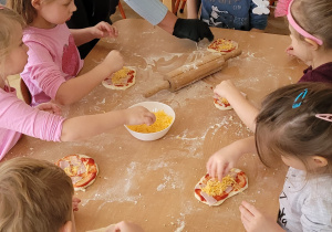 Dzieci nakładają składniki na pizzę - szynkę i ser.