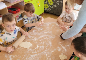 Dzieci dzieci rozciągają i rozwałkowują ciasto na pizzę.
