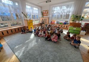 Dzieci siedzą na dywanie i oglądają film edukacyjny o Motylu.