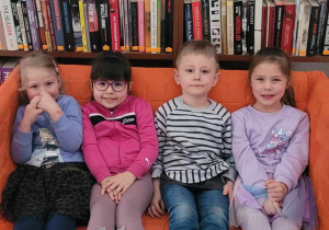 Dzieci siedzą na kanapie między regałami z książkami.