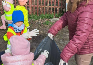 Dzieci wrzucają do worka pozbierane śmieci.