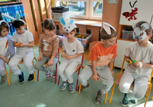 Dzieci siedząc na krzesełkach, otwierają kapsułki w których ukryta jest karteczka z napisaną liczbą.