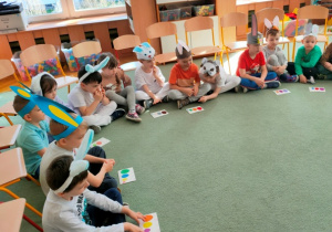 Dzieci siedzą na dywanie w siadzie skrzyżnym, przed sobą kładą odnalezioną kartę z zadaniem.