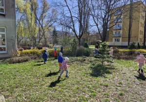 Dzieci szukają ukrytych jajek w ogrodzie przedszkolnym.
