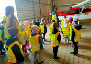 Dzieci oglądają samoloty szkoleniowe stacjonujące w hangarze.