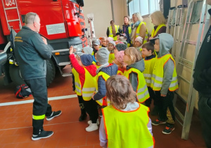 Dzieci słuchają wypowiedzi strażaka, który opowiada o swojej pracy.
