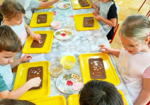 Dzieci układają słodkie dekoracje na masie czekoladowej.