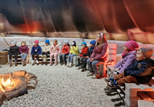 Dzieci siedzą w indiańskim tipi przy ognisku.