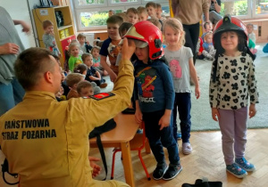 Dzieci prezentują się w hełmach strażackich.