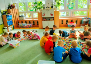 Dzieci siedzą na dywanie w dwóch zespołach i oglądają klocki GAMI, poznają sposób budowania z nich form przestrzennych.