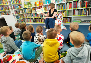 Dzieci słuchają bajki czytanej przez panią bibliotekarkę.