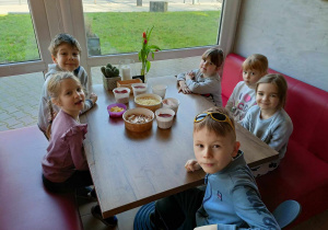 Grupa dzieci czekających przy stoliku na pizze.