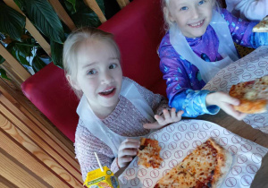 Uśmiechnięte dziewczynki degustują pizze.