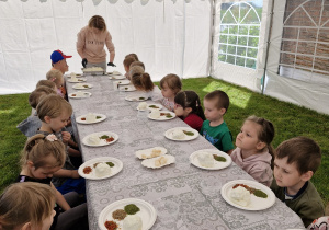 Pani Monika rozdaje ser kozi, z którego dzieci stworzą serowe kulki.