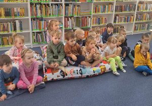 Dzieci siedzą na poduszkach i słuchają książeczki na temat instrumentów.