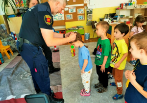 Przedstawiciel Straży Miejskiej kolejno każdemu dziecku wręcza medal "Bezpieczne dziecko".