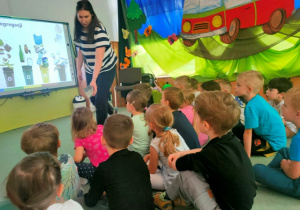 Pani pokazuje dzieciom jak zbudowane jest opakowanie po napojach, wskazuje do którego pojemnika powinno trafić to opakowanie.