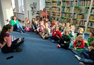 Dzieci siedzą na poduchach w czytelni. Pani bibliotekarka rozmawia z dziećmi.