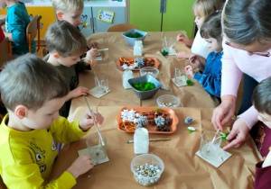 Dzieci ozdabiają szklane pojemniki materiałem przyrodniczym.