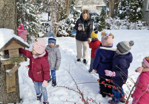 Dzieci dokarmiają ptaki w przedszkolnym ogrodzie.