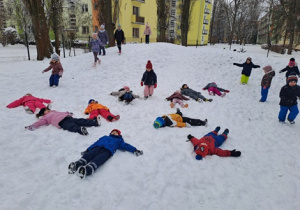 Dzieci robią aniołki na śniegu.