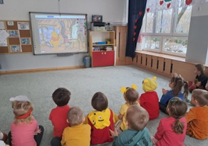 Dzieci siedzą na dywanie i oglądają na tablicy multimedialnej bajkę o Kubusiu Puchatku.