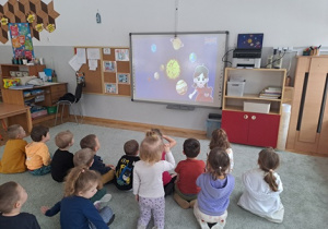 Dzieci oglądają film edukacyjny o planetach pod tytułem "Ala i układ słoneczny".