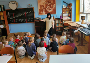 Nauczycielka muzyki rozmawia z dziećmi. Pokazuje im batutę, która jest nieodłącznym atrybutem dyrygenta.