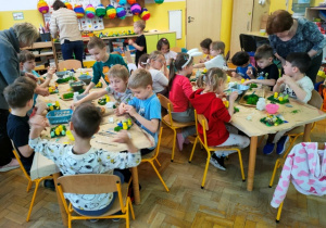 Dzieci pracują przy stolikach na których rozłożone są elementy dekoracyjne plastyczne.